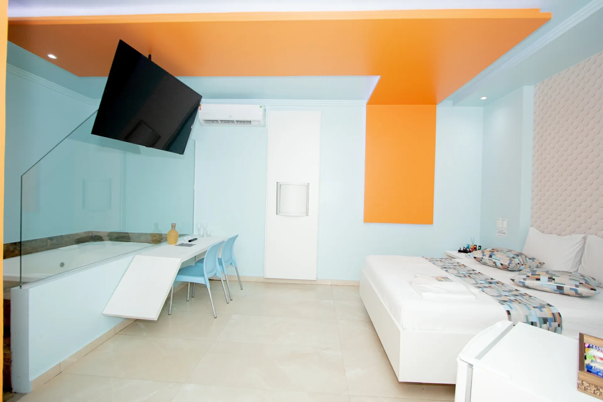 Suíte Hidro Plus do Motel Opium em Boa Vista: Visão geral grande-angular da suíte Hidro: cama branca à direita com almofadas pixeladas e parede 3D, banheira