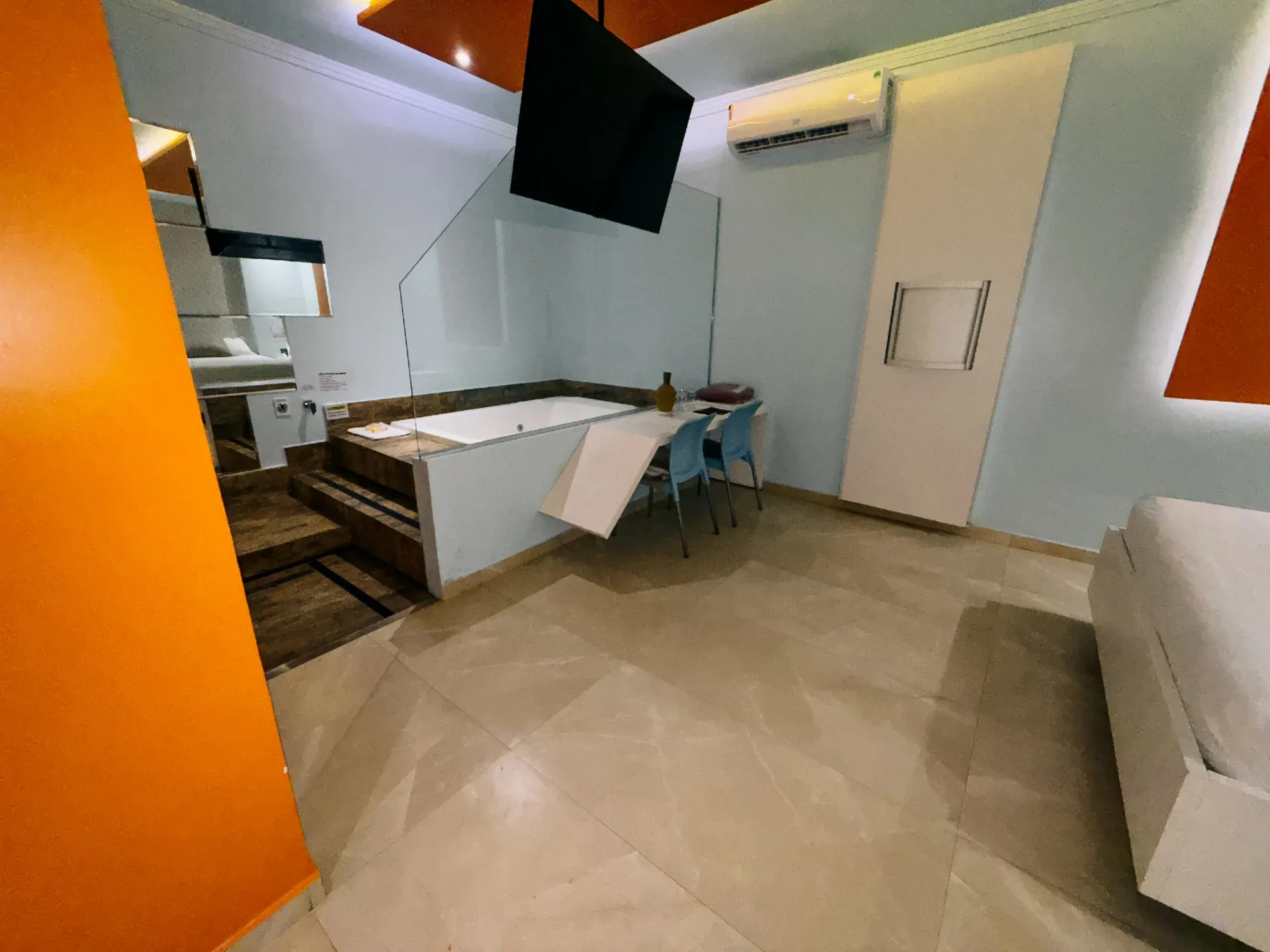 Suíte Hidro Plus do Motel Opium em Boa Vista: Suíte de categoria mais simples com paredes laranja e azul-claro: banheira de hidromassagem branca retangular 