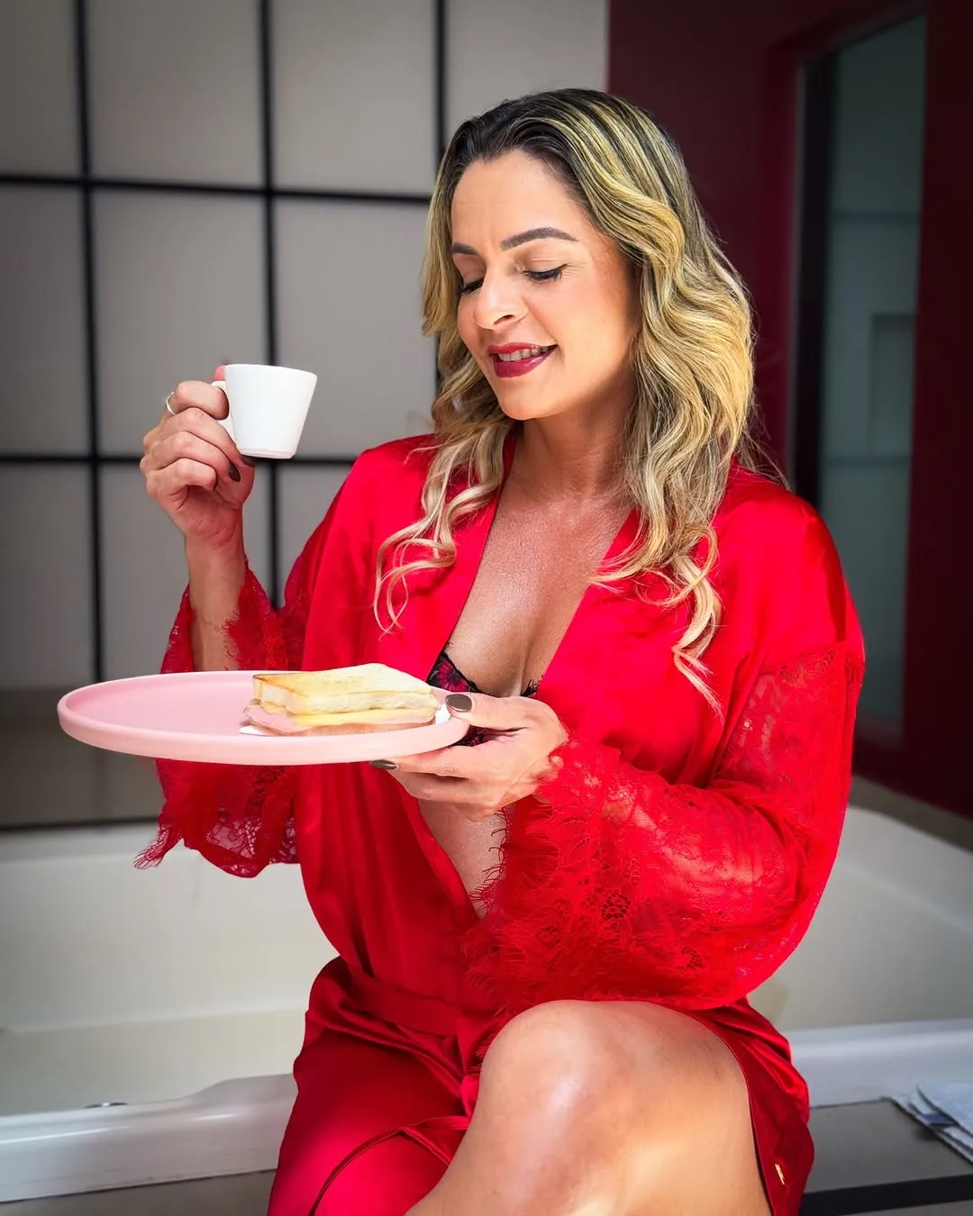 Motel Opium: Modelo loira de robe de cetim vermelho com renda segura xícara branca de café e prato rosa com misto quente, s