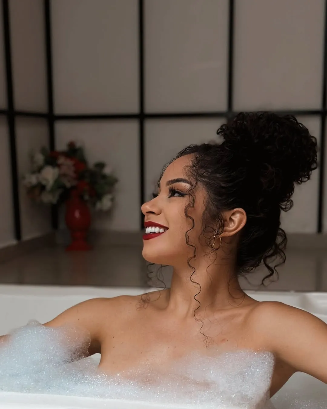 Motel Opium: Mulher de coque cacheado e batom vermelho sorrindo de perfil em banheira repleta de espuma