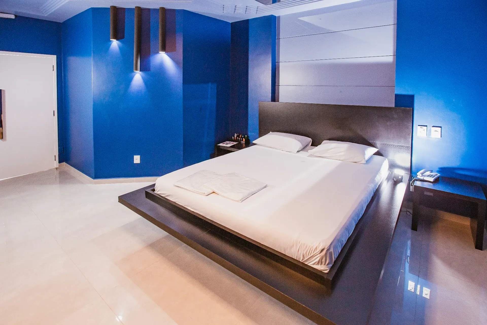 Suíte Luxo do Motel Opium em Boa Vista: Quarto da suíte Luxo: cama plataforma flutuante preta estilo japonês com lençóis brancos, cabeceira em painel 