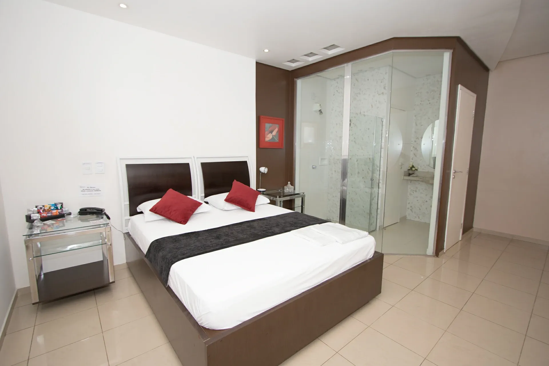 Suíte Luxo do Motel Opium em Boa Vista: Suíte em marrom-chocolate e branco: cama de madeira escura com cabeceiras duplas, almofadas vermelhas e manta 