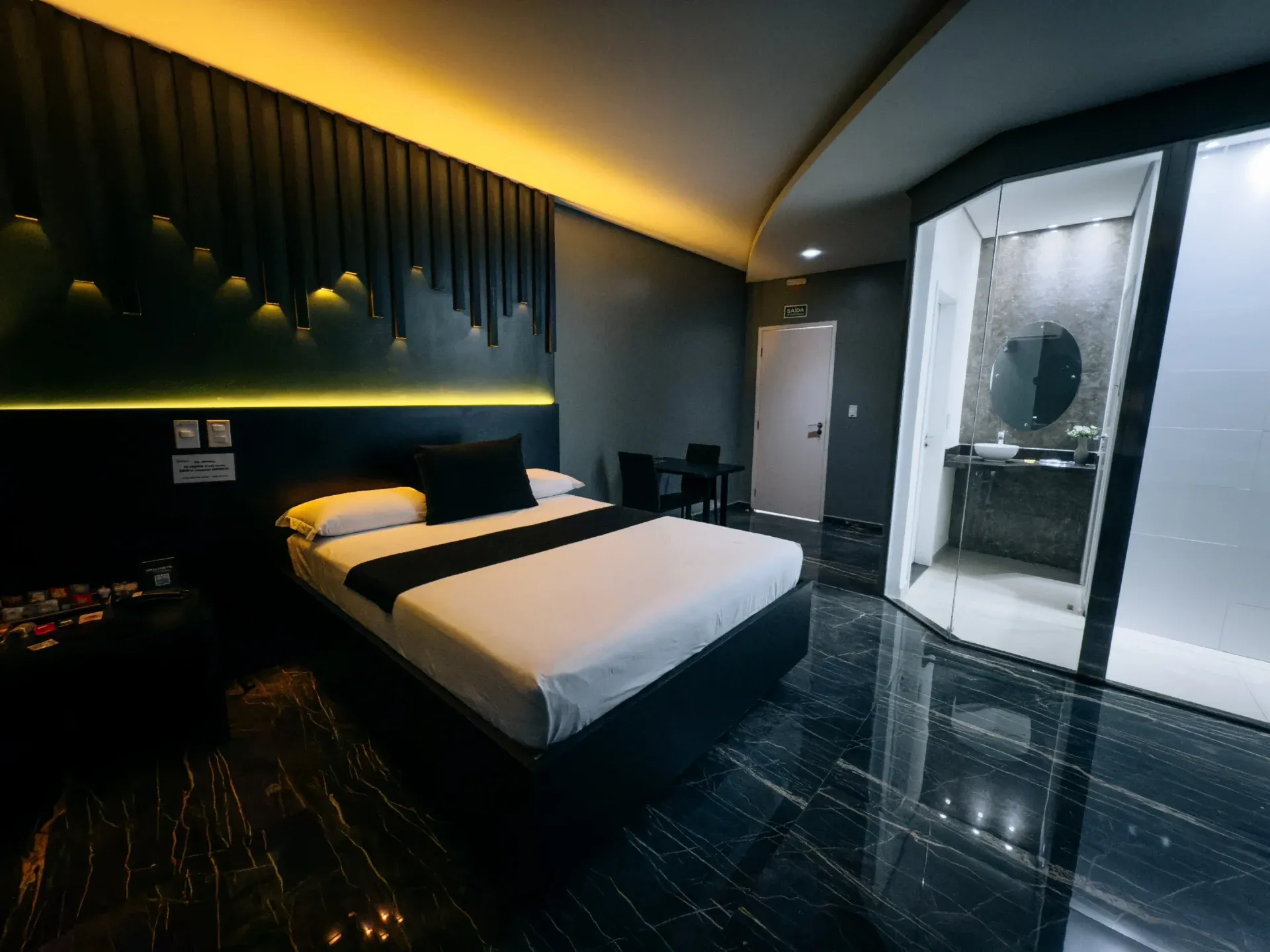 Suíte Luxo do Motel Opium em Boa Vista: Cama queen com base flutuante preta, painel de ripas iluminado com LED dourado, piso de mármore preto brilhant