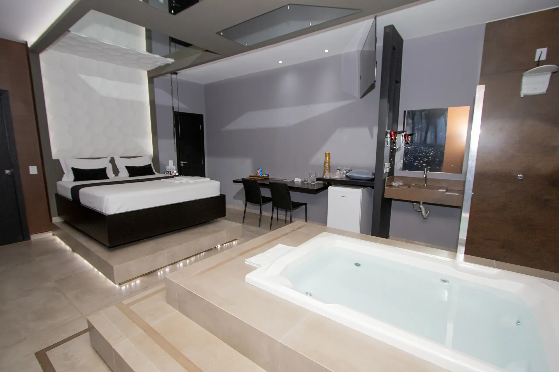 Suíte Luxo Hidro do Motel Opium em Boa Vista: Suíte premium em tons de bege, cinza e marrom: cama em plataforma elevada com fita de LED no rodapé, painel de