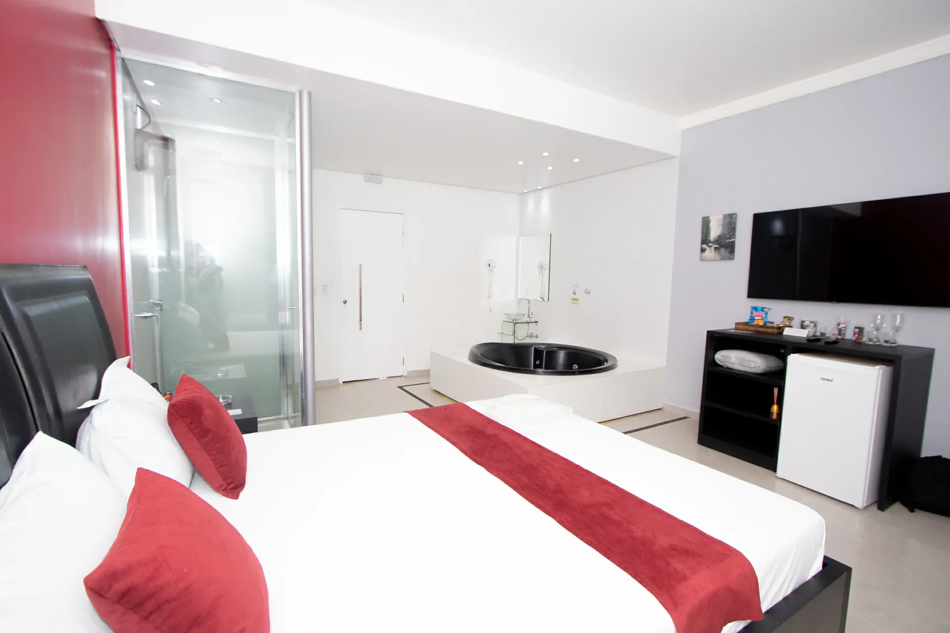 Suíte Luxo Hidro do Motel Opium em Boa Vista: Mesma suíte vermelha fotografada de cima da cama: almofadas e peseira vinho em primeiro plano, cabeceira de co