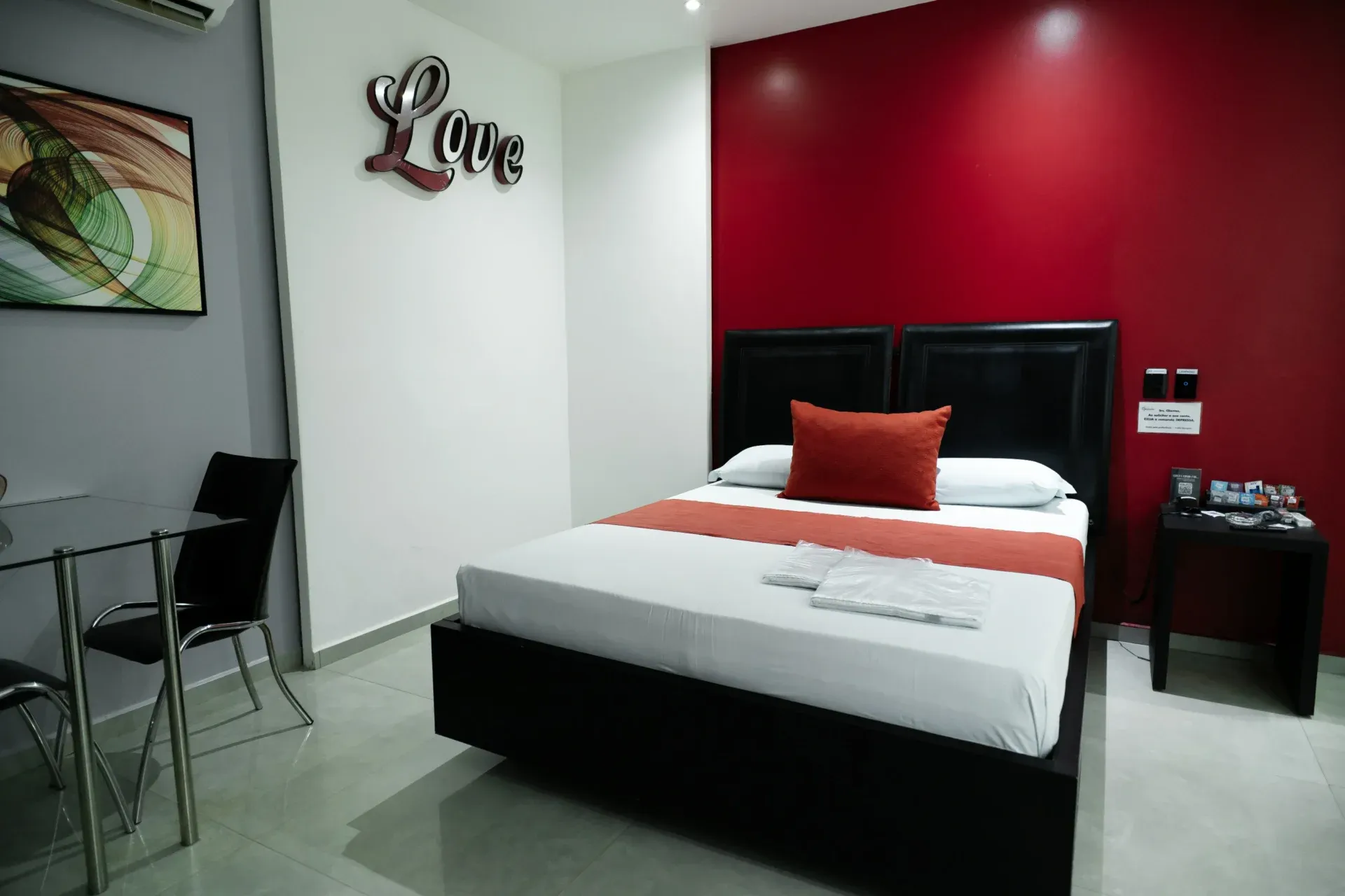 Suíte Luxo Hidro do Motel Opium em Boa Vista: Suíte básica com parede de destaque vermelho vinho, cama de casal box com cabeceira dupla estofada preta, faix