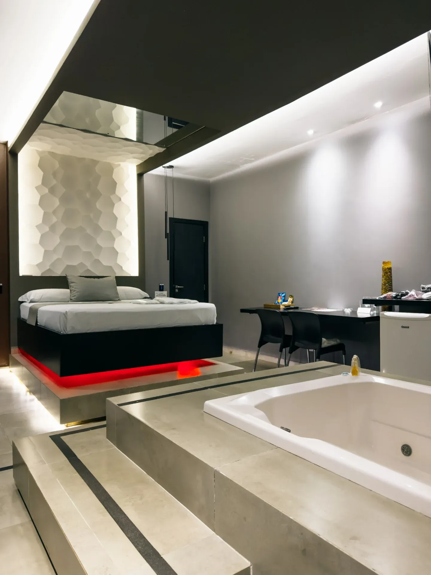 Suíte Luxo Hidro do Motel Opium em Boa Vista: Cama flutuante em base preta com LED vermelho embaixo, painel de cabeceira 3D hexagonal branco retroiluminado,