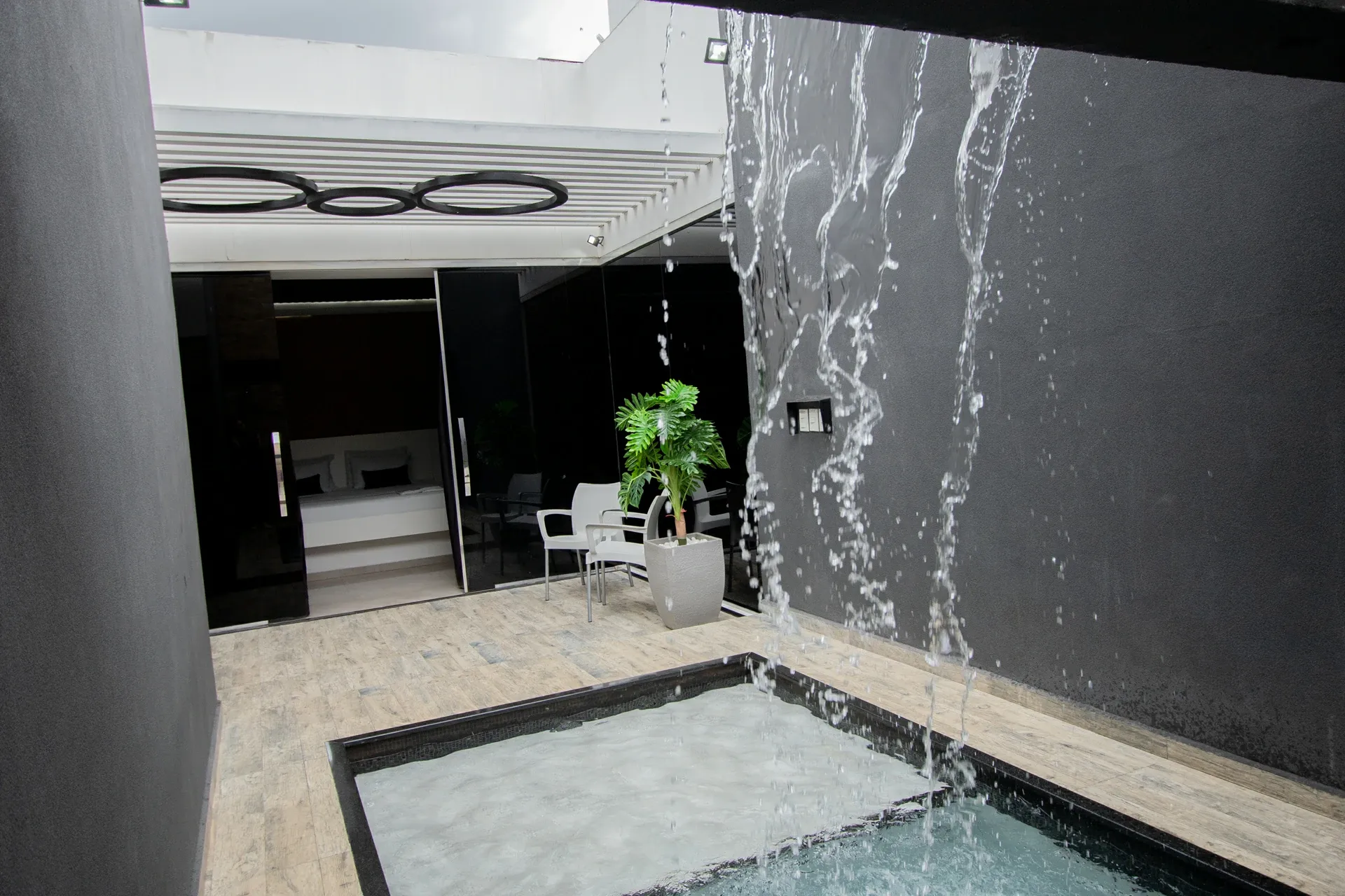 Suíte Opium do Motel Opium em Boa Vista: Água congelada em pleno ar em primeiro plano, revelando o pátio privativo com piscina, paredes grafite, pérgol