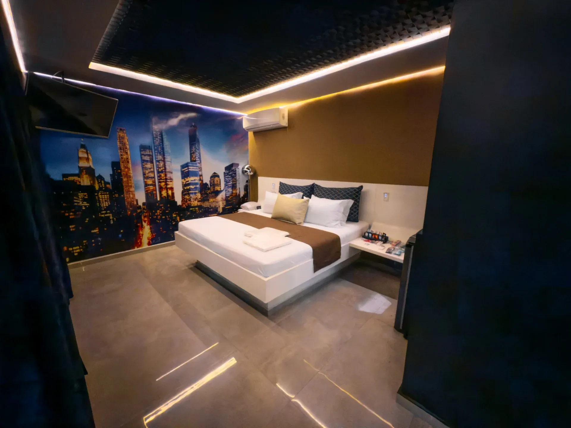 Suíte Opium do Motel Opium em Boa Vista: Quarto de suíte com cama box casal branca (roupa branca com manta marrom e almofadas azul-marinho), mural foto