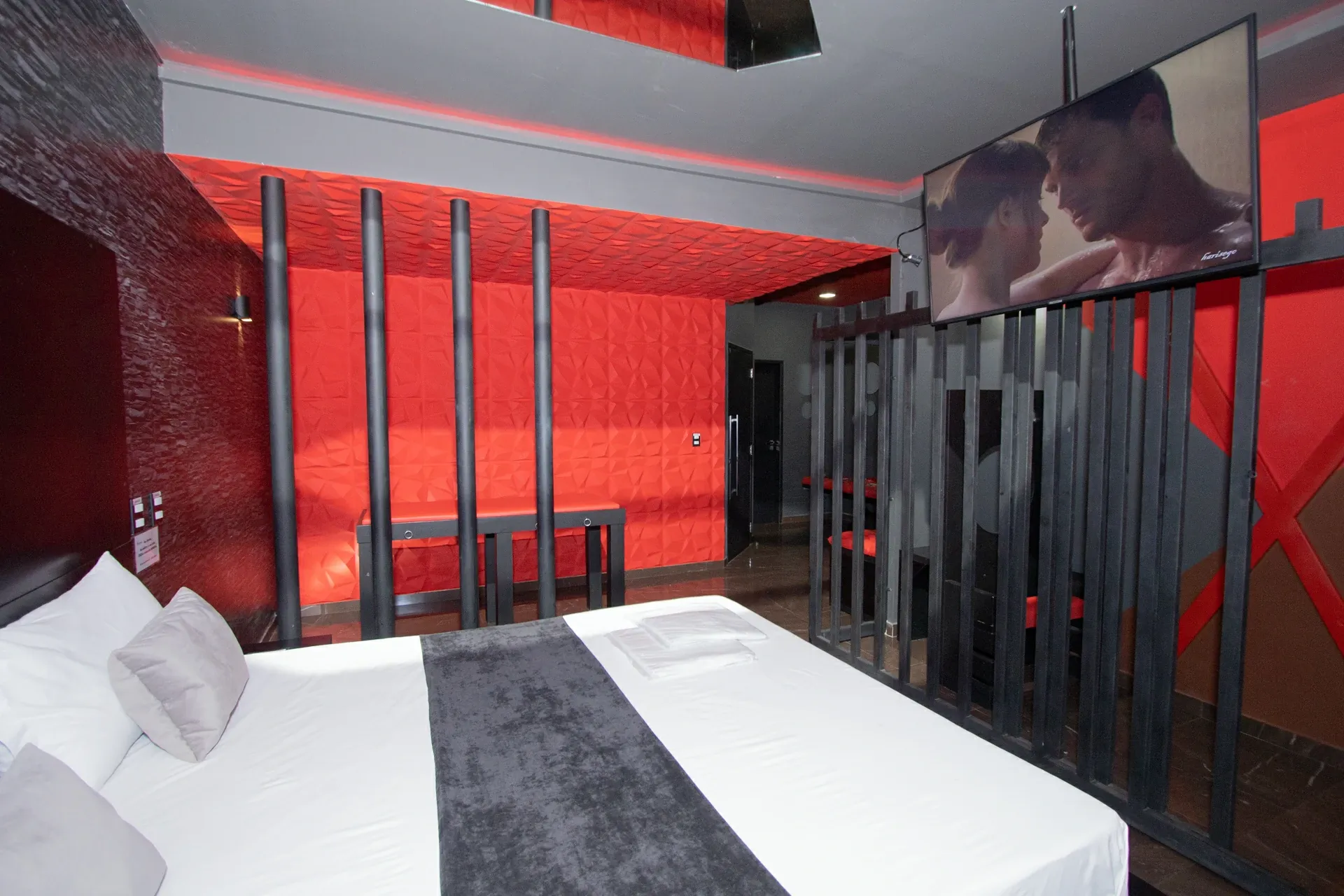 Suíte Sado do Motel Opium em Boa Vista: Suíte temática Sado em vermelho e preto: cama com colcha branca e passadeira de veludo grafite, parede de pedr