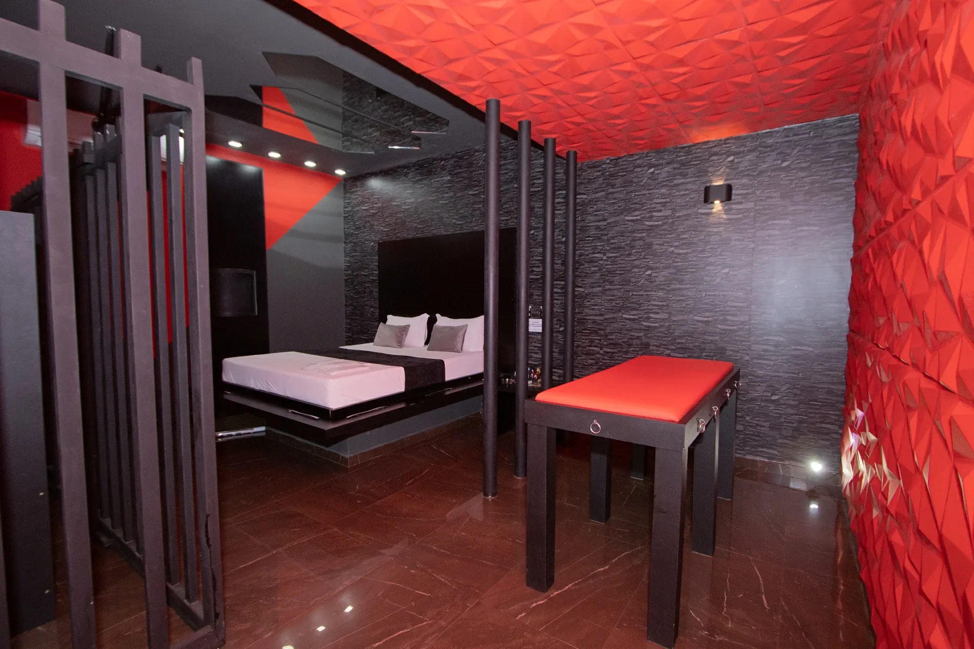 Suíte Sado do Motel Opium em Boa Vista: Teto e parede direita em revestimento 3D diamante vermelho vivo, parede de pedra canjiquinha grafite, cama flu