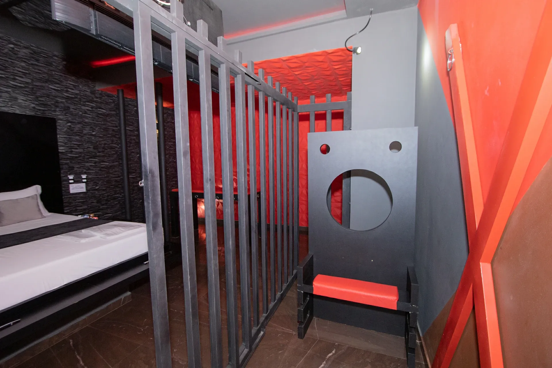 Suíte Sado do Motel Opium em Boa Vista: Detalhe da área de 'cela' da suíte BDSM: grade de barras quadradas pretas em primeiro plano e pelourinho/tronc