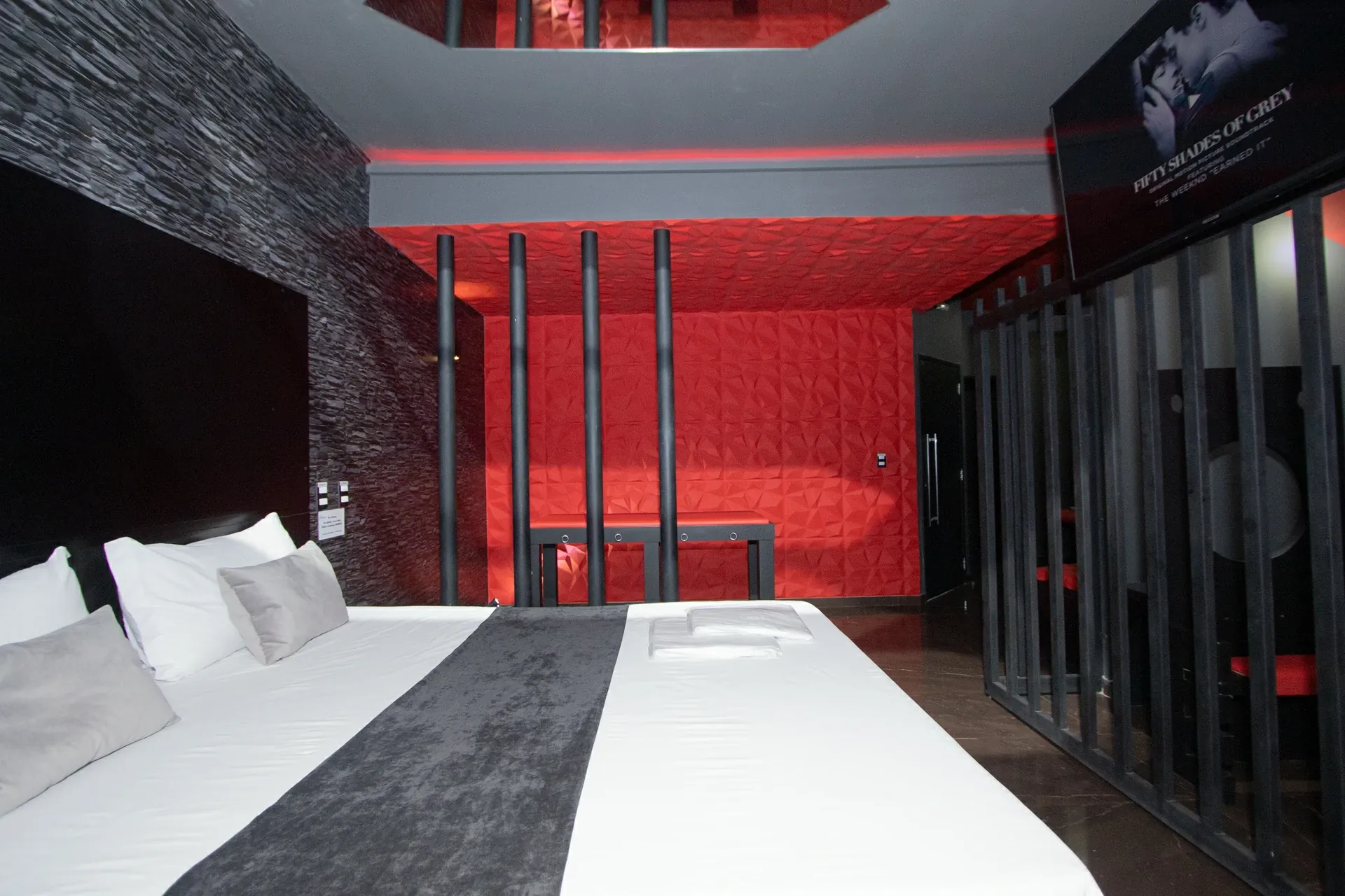 Suíte Sado do Motel Opium em Boa Vista: Cama king de plataforma preta com roupa branca e xale de veludo cinza, parede de pedra preta, parede e teto em