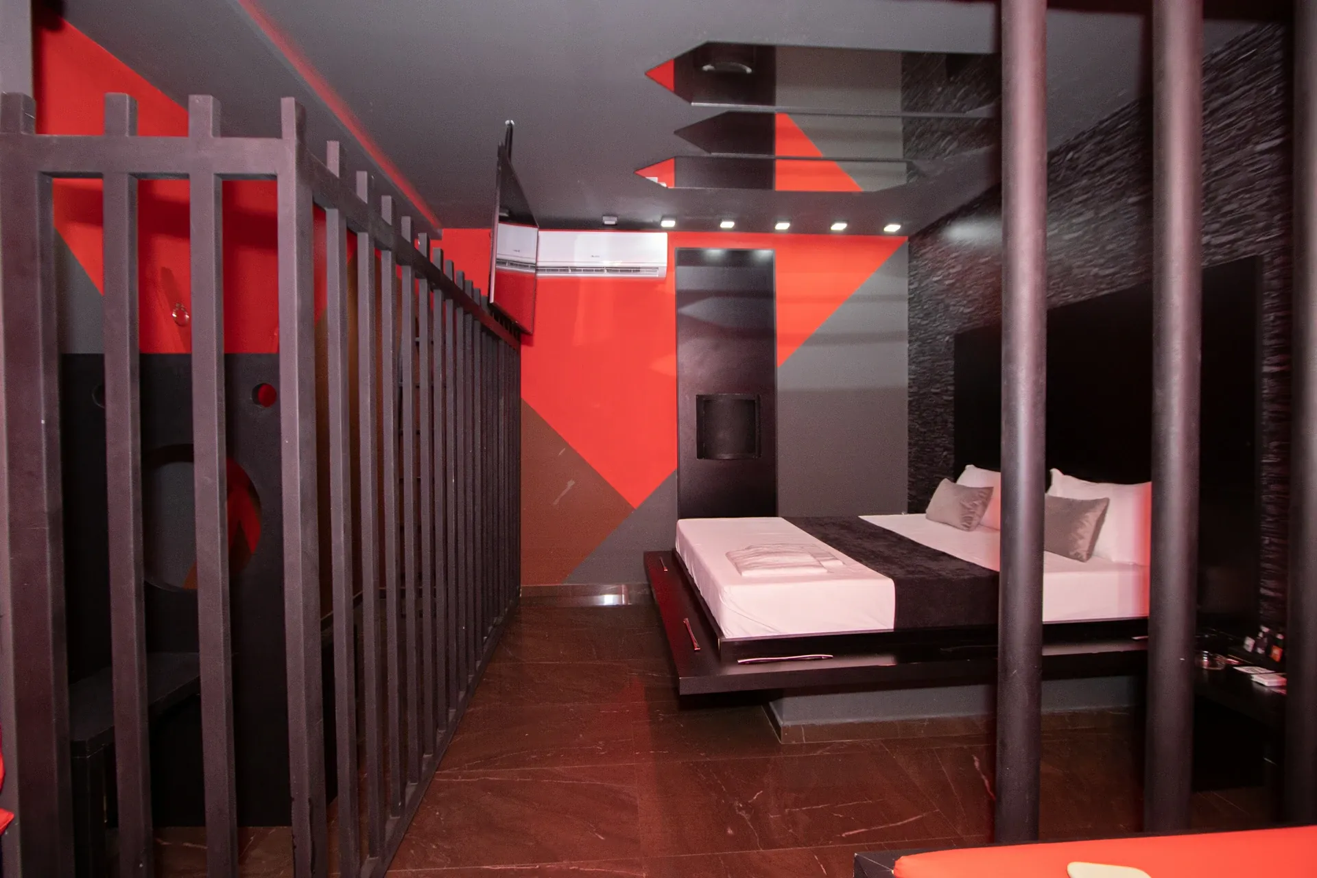Suíte Sado do Motel Opium em Boa Vista: Corredor interno da suíte Sado fotografado por entre as grades da 'cela': barras pretas dos dois lados, TV na 
