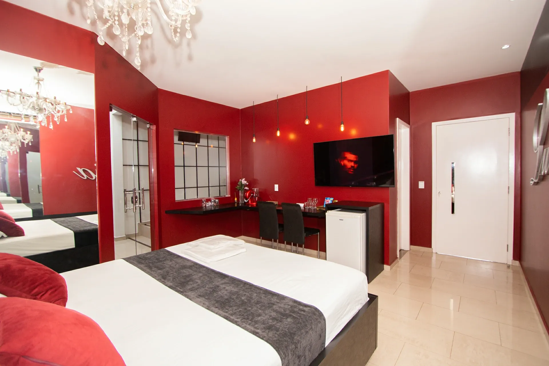 Suíte VIP do Motel Opium em Boa Vista: Cama king com roupa branca e manta cinza-grafite, paredes vermelho profundo, lustre de cristal, parede espelha