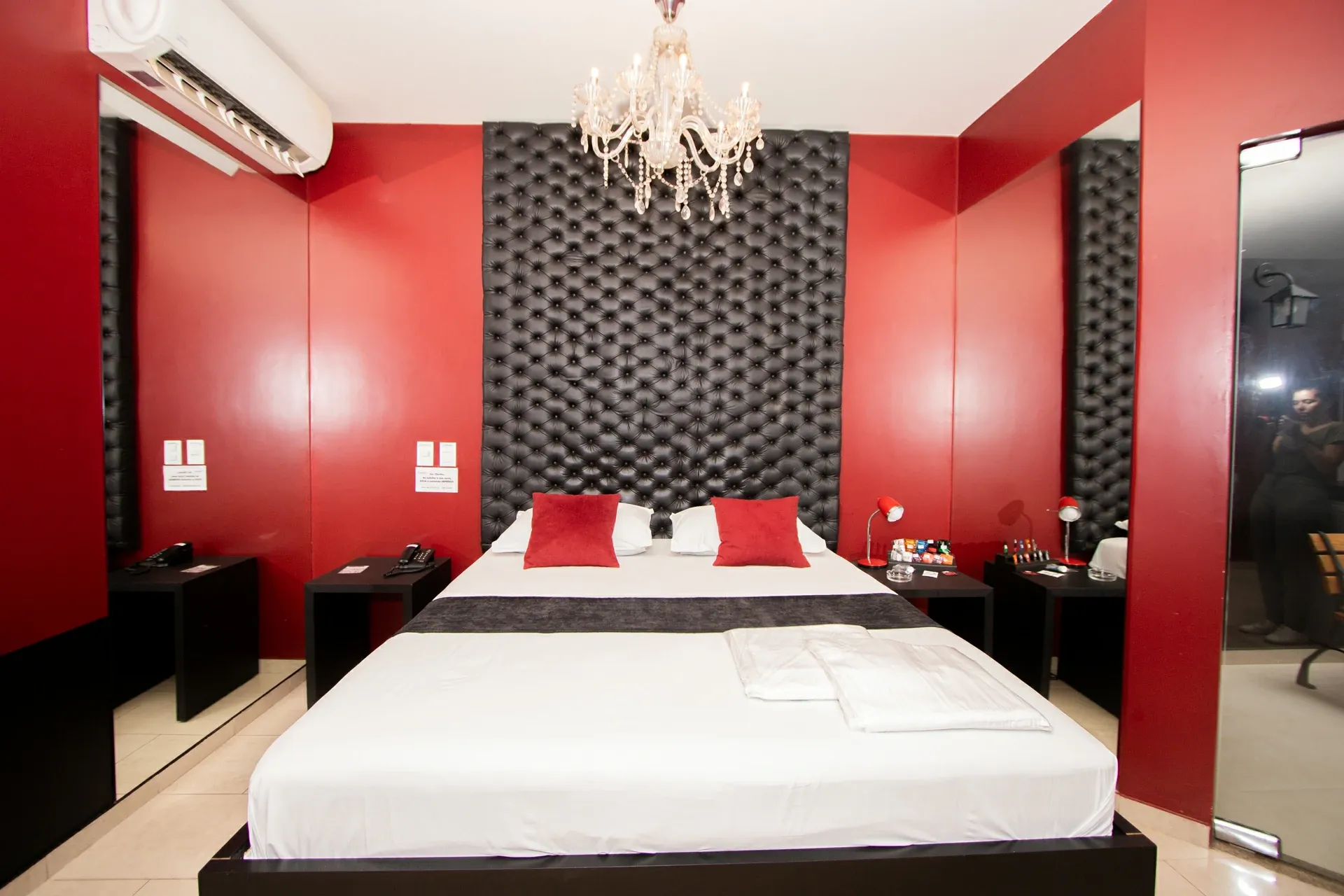 Suíte VIP do Motel Opium em Boa Vista: Enquadramento frontal simétrico da cama king da suíte vermelha: cabeceira capitonê preta de altura total até o