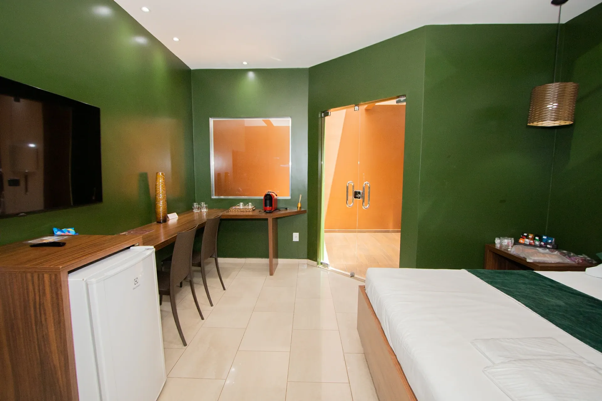 Suíte VIP do Motel Opium em Boa Vista: Suíte de paleta verde-oliva com marcenaria em madeira: TV na parede, frigobar Electrolux, bancada-escrivaninha