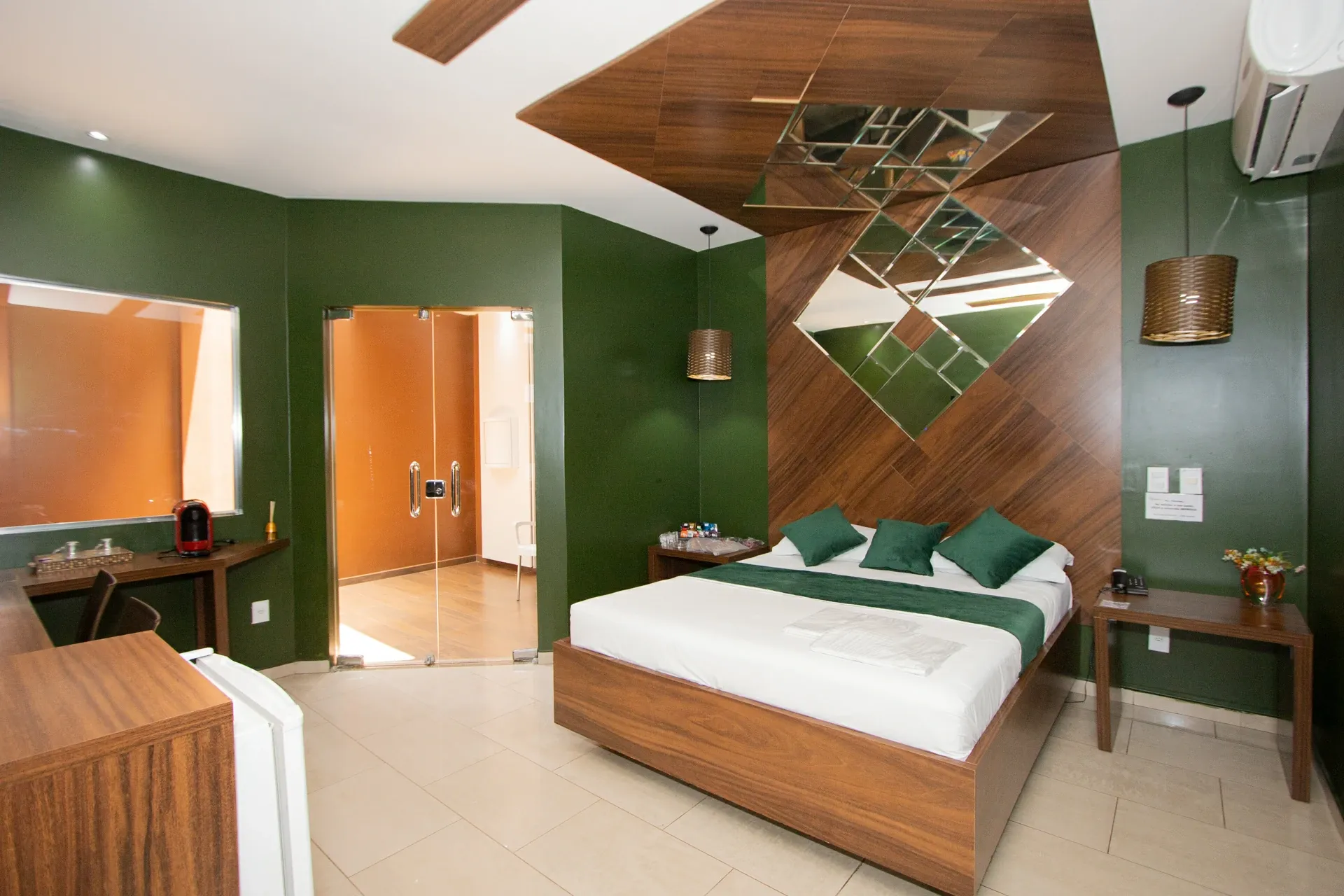 Suíte VIP do Motel Opium em Boa Vista: Suíte com paredes verde-musgo e painel de madeira em diagonal que sobe da cabeceira ao teto, com composição de