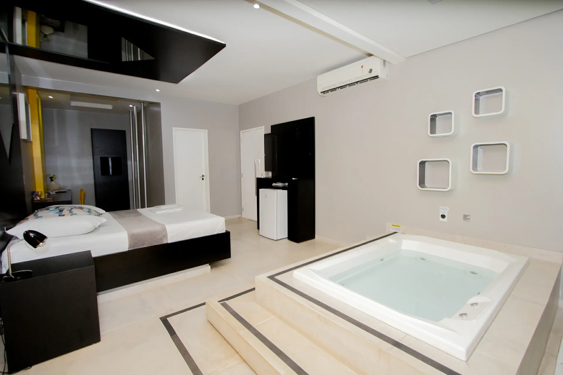 Suíte VIP do Motel Opium em Boa Vista: Mesma suíte preto/amarelo vista do ângulo oposto: hidromassagem quadrada branca sobre plataforma com degraus e