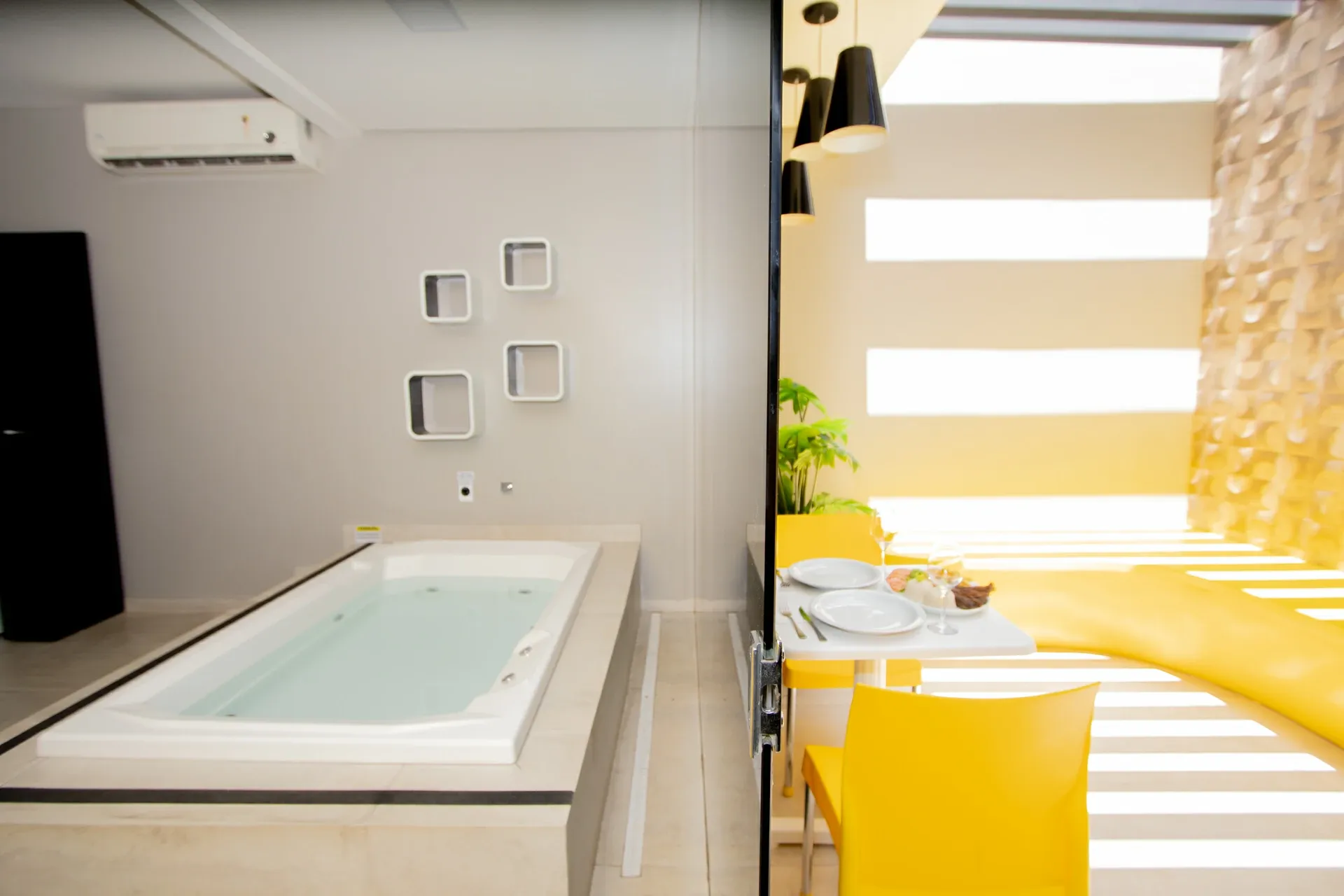 Suíte VIP do Motel Opium em Boa Vista: À esquerda, banheira de hidromassagem branca sobre plataforma com nichos quadrados decorativos na parede cinza