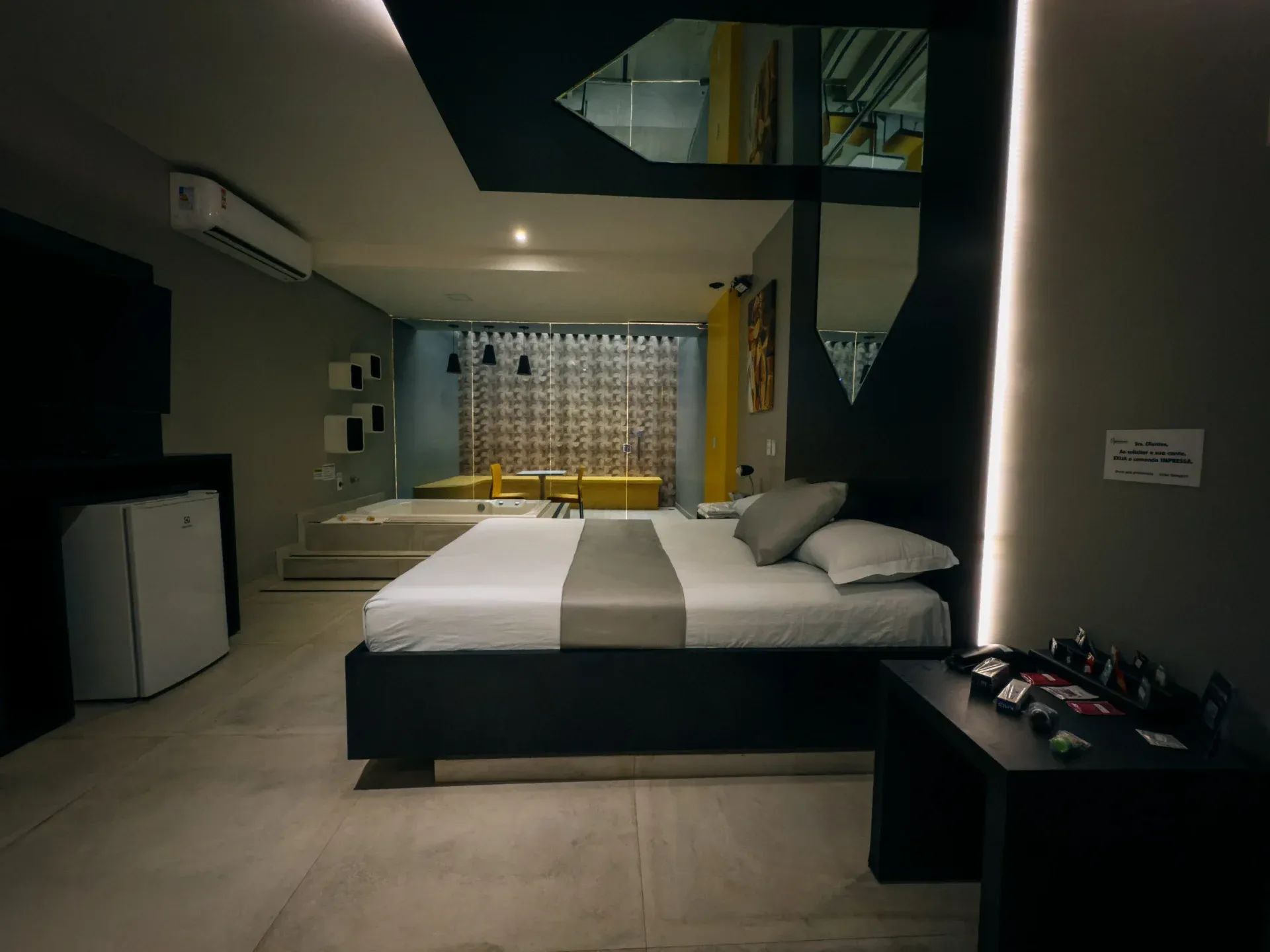 Suíte VIP do Motel Opium em Boa Vista: Suíte moody em preto, cinza e amarelo: cama king de base preta com faixa cinza, espelho facetado no teto sobre