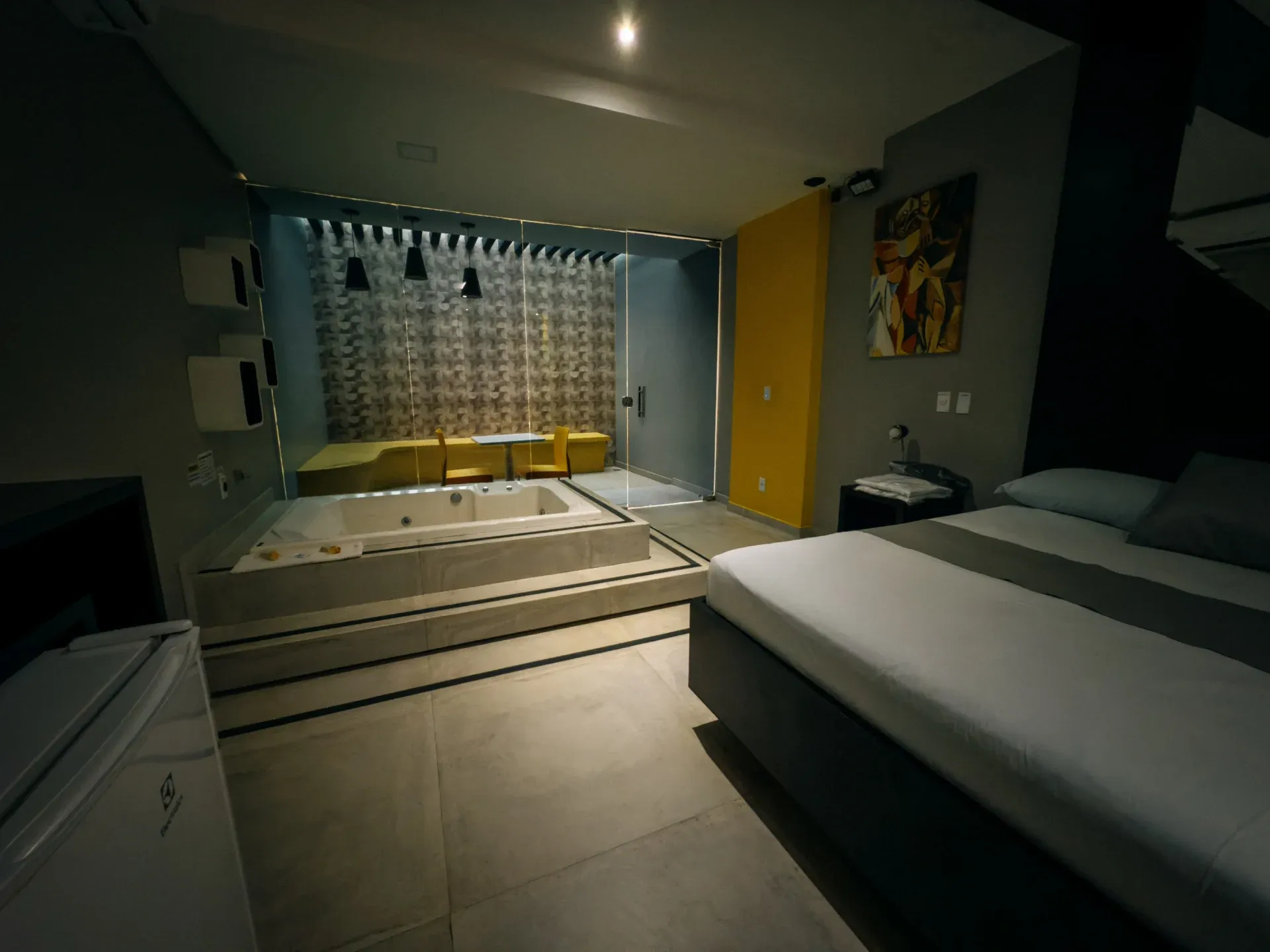 Suíte VIP do Motel Opium em Boa Vista: Mesma suíte preto/amarelo por outro ângulo: cama à direita, hidromassagem branca em plataforma elevada com deg
