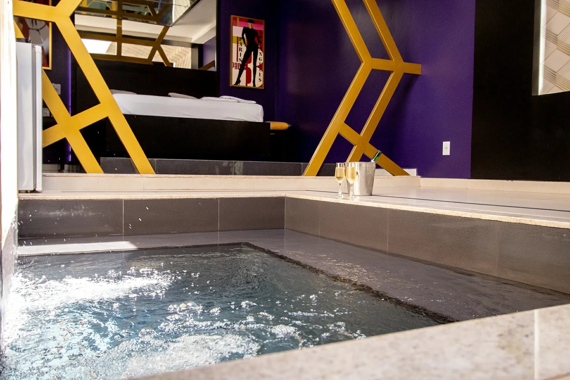 Suíte VIP Plus do Motel Opium em Boa Vista: Piscina de hidromassagem privativa revestida em porcelanato cinza com água borbulhando em primeiro plano, cham