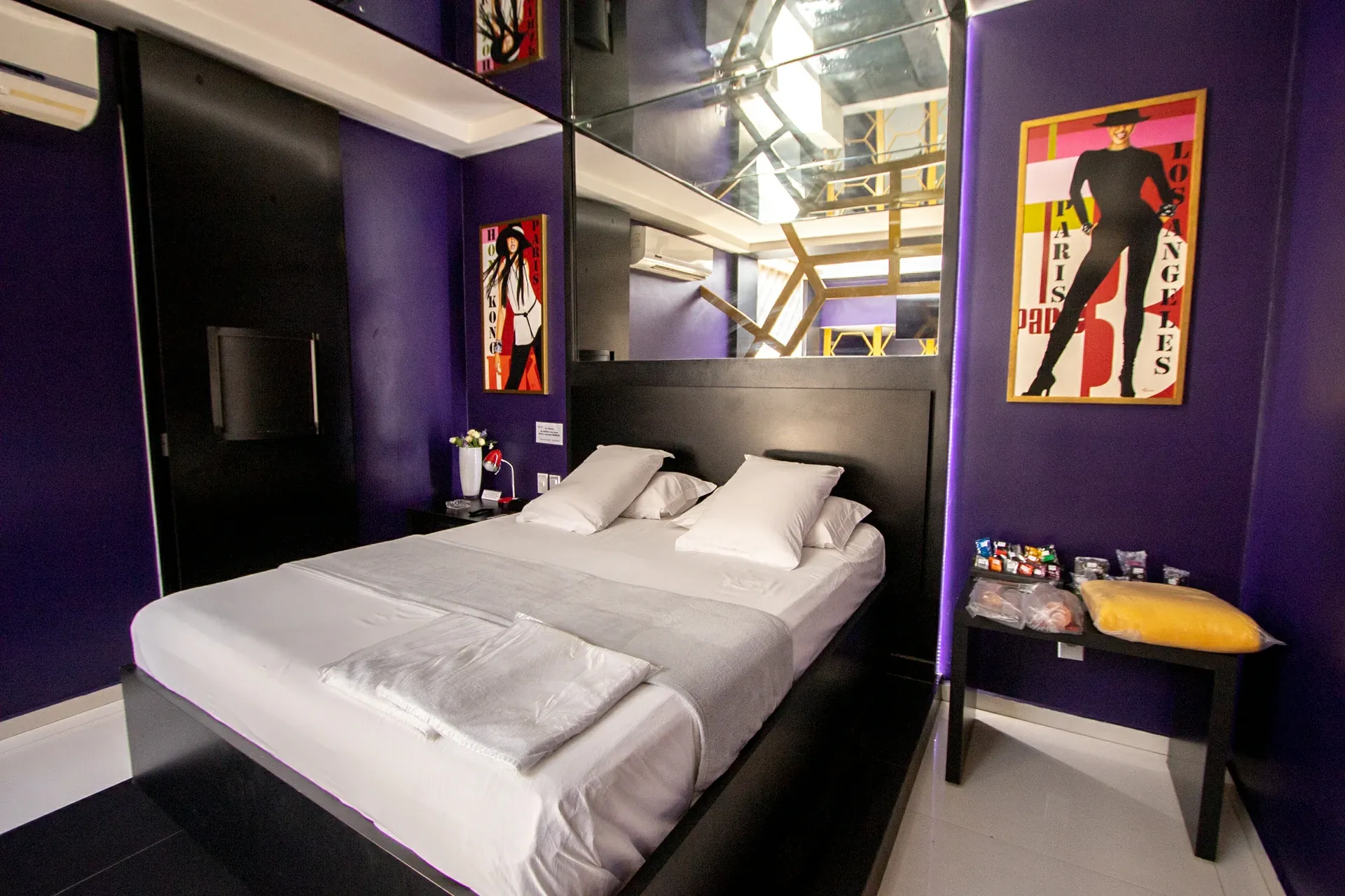 Suíte VIP Plus do Motel Opium em Boa Vista: Quarto da suíte VIP Plus em enquadramento frontal simétrico: cama de casal com cabeceira preta e roupa branca/