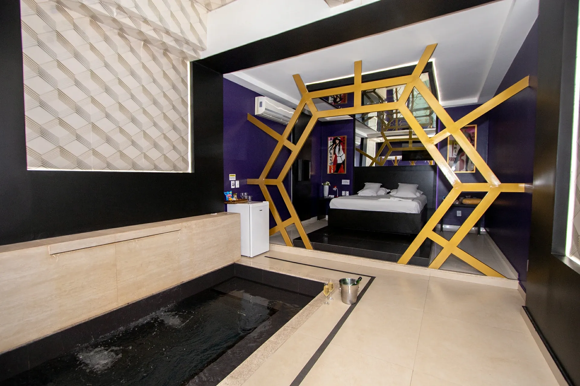 Suíte VIP Plus do Motel Opium em Boa Vista: Banheira embutida de azulejo preto com água borbulhando e balde de espumante com duas taças na borda, mureta d